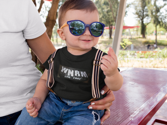 Super cute baby wearing a OG WNRM Boobs baby by T-Shirt, with sunglasses and suspenders on, on a red picnic table