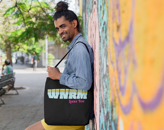 Cool guy holding a WNRM Loves You Polyester Canvas Tote Bag, outside next to graffiti art 