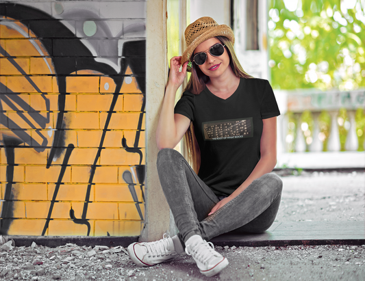 Pretty, young woman, wearing a WNRM Name In Lights Tee, wearing a hat and sunglasses next to  graffiti art and trees on a sunny day 
